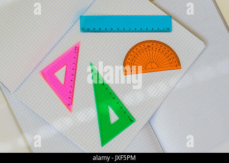 Close-up of set of colored instruments for geometry on background of large open empty notebooks in a cage, top view, texture. Place for text, concept of starting school, back to school, any new cases Stock Photo