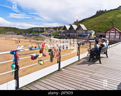 dh Saltburn pier SALTBURN BY THE SEA CLEVELAND People sitting relaxing on seaside pier knitted yarn bombing sea figures uk Stock Photo