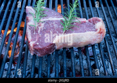 T-bone steak cooking on an open flame grill , with rosemary and salt Stock Photo
