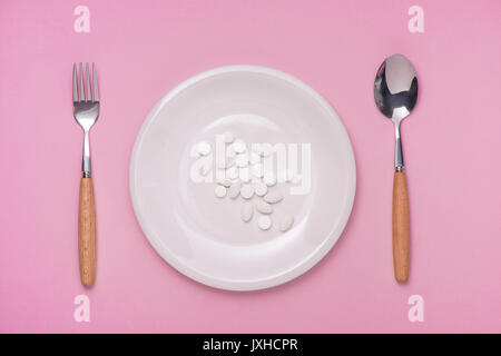 Pills served as a healthy meal. Drug capsule on white plate on pink background Stock Photo