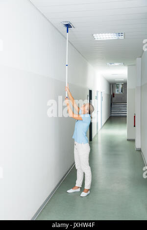 Young Woman Cleaning The Ceiling With Mop On The Corridor Of The Building Stock Photo