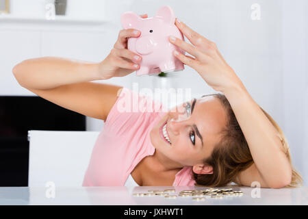 Young Happy Woman Emptying Her Piggybank Savings With Less Than Expected At Home Stock Photo