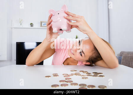 Young Happy Woman Emptying Her Piggybank Savings With Less Than Expected At Home Stock Photo