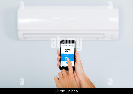 Woman Hand Setting Temperature Of Air Conditioner Using Smartphone App At Home Stock Photo