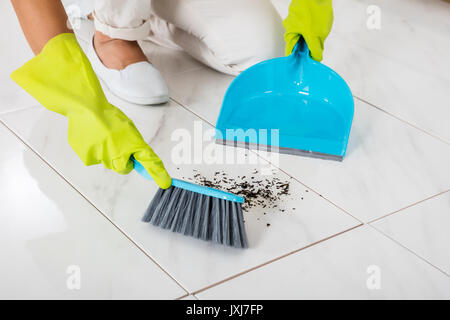 Close-up Of Person Hand Wearing Gloves Using Broom And Dustpan On The Floor Stock Photo
