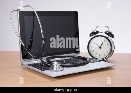 Side view of black and silver medical stethoscope on laptop computer next to black and white alarm clock Stock Photo