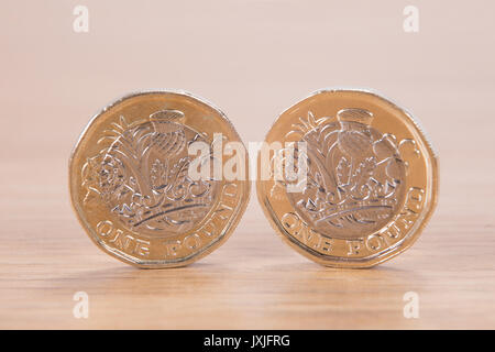 Two pound coins balancing on edge on a wooden table showing the engraving and design on the new money in a financial concept