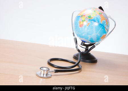 Side view of black and silver stethoscope attached to miniature plastic toy globe sitting on brown wooden surface Stock Photo