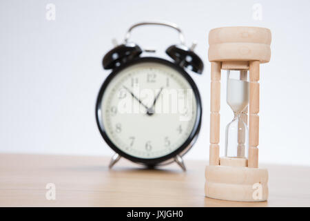 Small wooden egg timer with an alarm clock on a wooden table with focus to the sand pouring through the bulbs as it counts down to a deadline Stock Photo