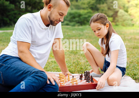 Little daughter playing chess with her father outdoors Stock Photo