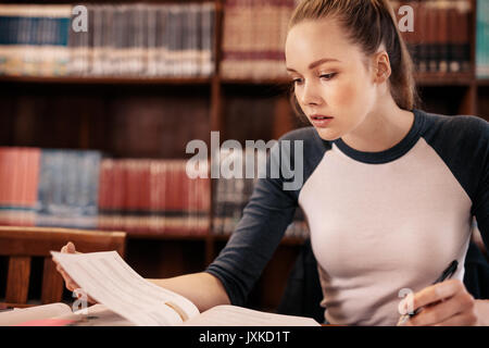 Young student learning from book in the library. university female student preparing notes for the exam in library. Stock Photo