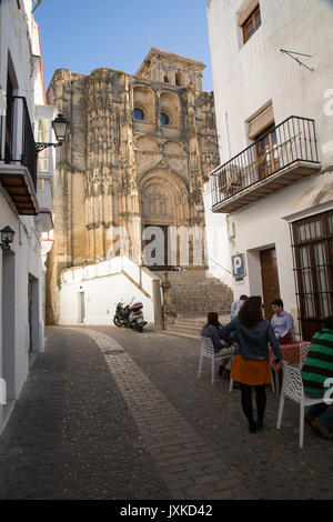 Narrow street cafe and church of Santa Maria de la Asuncion, Arcos de la Frontera, Cadiz province, Spain Stock Photo