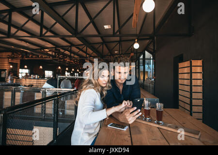 Young man and woman at the bar using mobile phone. Friends in a bar looking at cell phone. Stock Photo
