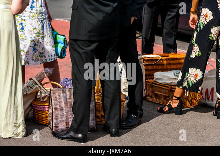 Young opera fans with picnic baskets wait to board a bus to Glyndebourne Opera House for a performance of Don Pasquale, Lewes, Sussex, UK Stock Photo