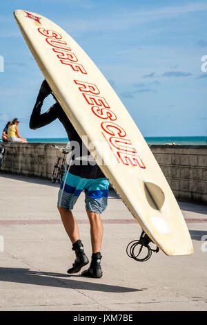 A Man Takes His Surf Board On To The Beach, Rottingdean, East Sussex, UK Stock Photo