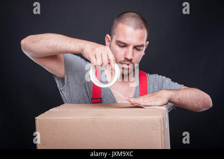 Mover guy packing carefully box with duct tape on black background Stock Photo