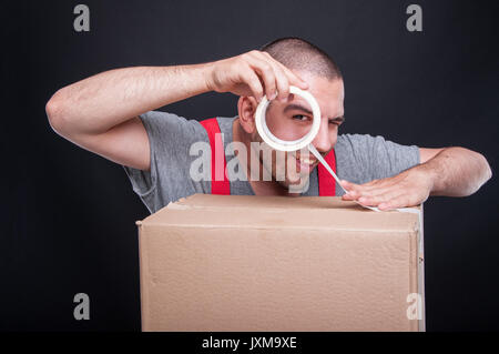 Mover guy packing box with duct tape being playful and smiling on black background Stock Photo