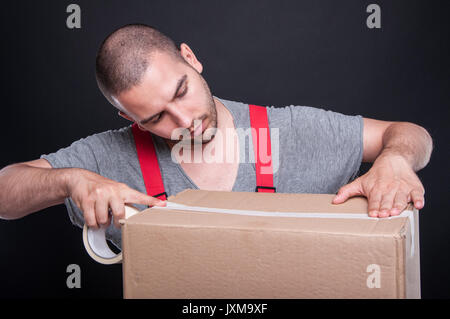 Mover guy packing carefully box with duct tape on black background Stock Photo