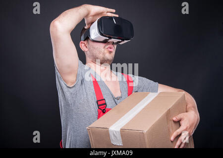 Mover guy holding box wearing vr glasses looking far away on black background Stock Photo