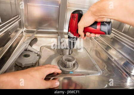 Close-up Of Repairman Fixing Dishwasher With Electric Drill Stock Photo