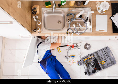 High Angle View Of Male Plumber In Overall Fixing Sink Pipe Stock Photo
