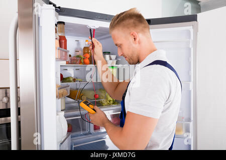 Young Repairman Checking Refrigerator With Digital Multimeter Stock Photo
