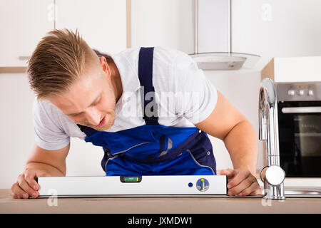 Male Plumber Measuring Level Of A Sink In Kitchen Stock Photo