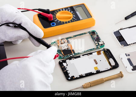Close-up Of Person's Hand Checking Mobile Phone With Digital Multimeter Stock Photo