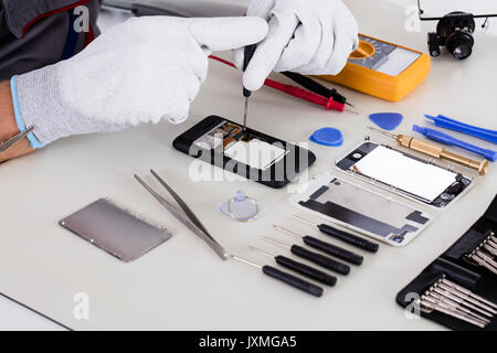 Close-up Of Person's Hand Using Screwdriver To Repair Mobile Phone Stock Photo