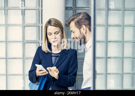 Businessman and woman looking at smartphone by glass wall in office Stock Photo