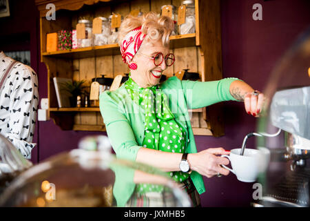Quirky vintage mature woman working behind tea room counter Stock Photo