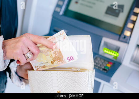 Close up of woman's hands inserting 50 euro notes into purse from cash machine Stock Photo