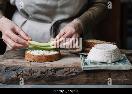 Woman placing slices of avocado onto sliced bread with ricotta, mid section Stock Photo