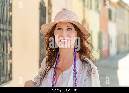 portrait of beautiful mature tourist with wide hat in a picturesque village in Europe, Caucasian woman with both Middle Eastern and American details Stock Photo