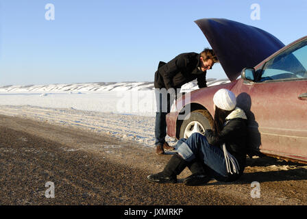 A couple are stranded at side of highway with a car breakdown in winter. Stock Photo