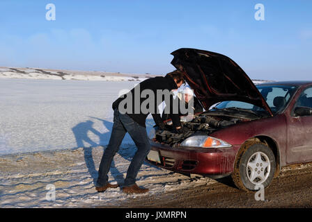 A stranded couple with broken down car on side of the road in winter Stock Photo