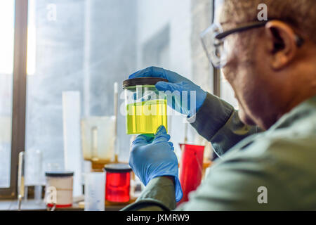 Lab technician inspecting beaker of yellow biofuel in biofuel plant laboratory Stock Photo