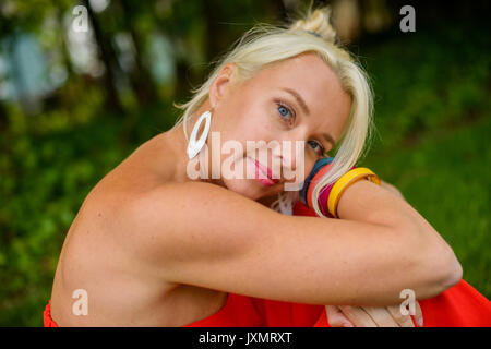 Portrait of blond haired woman in red sundress sitting in garden Stock Photo