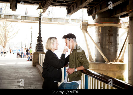 Young couple, standing underneath bridge, young woman touching man's face, smiling Stock Photo