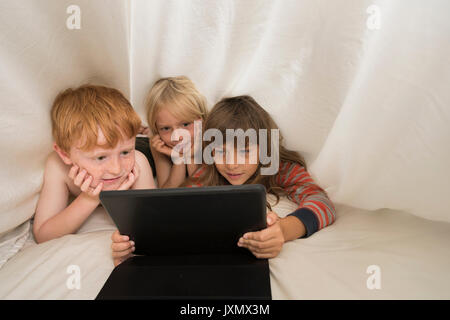 Children lying in bed looking at digital tablet Stock Photo