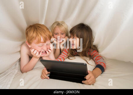 Children lying in bed looking at digital tablet Stock Photo