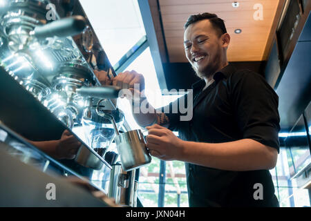 Young cheerful barista preparing coffee at an automatic machine 