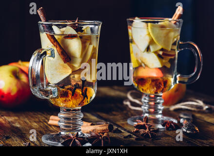 Two Glasses of Christmas Spiced Beverage with Sliced Apple, Clove, Cinnamon, Anise Star and Dark Candy Sugar. All Ingredients and Some Kitchen utensil Stock Photo