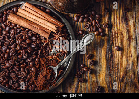 Coffee Beans with Spooonful of Ground Coffee, Cinnamon Sticks and Chinese Star Anise on Metal Plate. Some Beans Scattered on Wooden Table. View from A Stock Photo