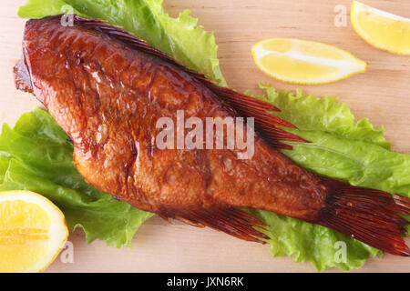Smoked fish and lemon on green lettuce leaves on Wooden cutting board isolated on white background. Stock Photo