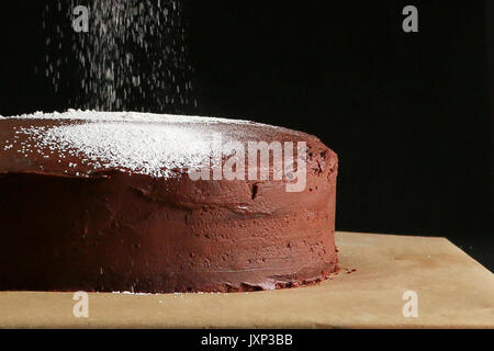 Tasty chocolate cake with falling icing sugar on dark background, close up. Stock Photo