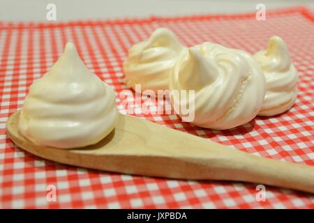 White meringues on a red and white cloth with a wooden spoon. Side view. Landscape format. Stock Photo