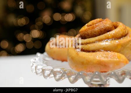 Cinnamon buns on an up stand plate with a blurred Christmas tree on the background. Side view. Landscape format. Stock Photo
