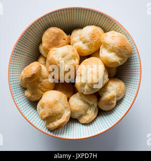 Top view of cream puffs in a blue dotted bowl on a white table. Squared format. Stock Photo