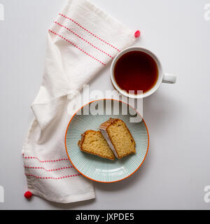 Cup of tea and two slices of sponge cake in a plate on a white table with a white and red tea towel. Top view. Square format. Stock Photo